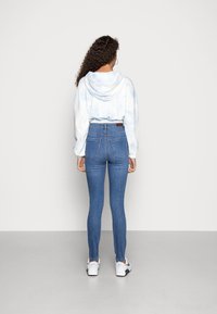 Sudadera tie-dye en azul claro con una gran capucha, combinada con jeans skinny azules de talle alto. Zapatillas blancas completan el atuendo.