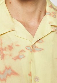 Korte mouwen shirt van lichtgele stof met een zachte textuur, voorzien van een subtiel abstract patroon in lichtoranje en blauw, met een enkele knoopsluiting.