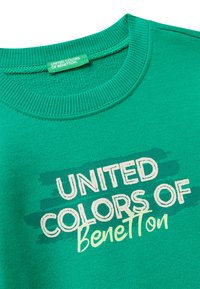 Zelená mikina s kulatým výstřihem vyrobená z měkké tkaniny, s bílým a tyrkysovým textem "UNITED COLORS OF Benetton" na texturovaném pozadí.