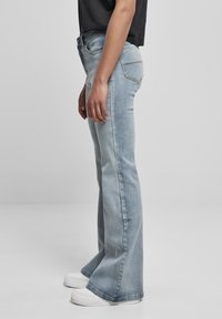 Ljusblå flare-jeans i denim med medelhög midja, synlig sömnad och sidofickor. Matchas med vita sneakers.