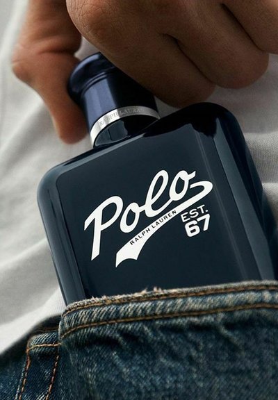 En mörkblå Polo Ralph Lauren-doftflaska är delvis nedstoppad i en denimficka, med en hand placerad ovanför.
