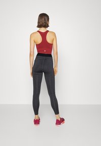 Czerwona sportowa koszulka na ramiączkach z tyłem w stylu racerback. Czarne legginsy z wysokim stanem w heatherowym wzorze. Różowe buty do biegania z pomarańczowymi podeszwami.