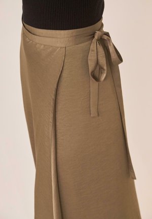 Falda marrón cruzada atada a la cintura combinada con un top negro de canalé, mostrada desde la cintura hasta el medio muslo sobre un fondo neutro.