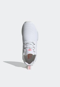 Zapatilla blanca con parte superior de malla texturizada, que presenta un patrón de rejilla. Diseño de cordones, logo rosa en la lengüeta y tirador en el talón.