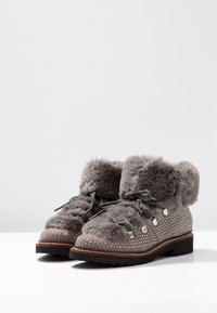 Bottes en fourrure grise, ornées de studs, à bout rond et à laçage. Elles disposent d'une tige texturée et d'une semelle en caoutchouc durable.