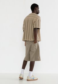 Kortærmet beige stribet skjorte og khaki shorts; skjorten har en afslappet pasform og struktureret stof; parret med beige sneakers og hvide sokker.