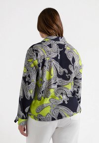 Blusa negra con detalles en verde lima con un diseño de paisley, de mangas largas y con cuello. Tejido suave y ligero.