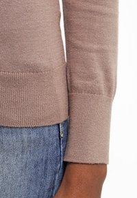 Ljusbrun stickad tröja med ribbade muddar. Materialet ser mjukt och texturerat ut, vilket passar bra med blå denim, och ger en avslappnad stil.