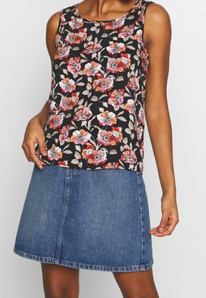 Kvinde iført en ærmeløs sort top med pink og orange blomsterprint og en blå denim nederdel.