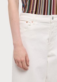 Hvit denim bukser med rett passform, med kobberknappdetaljer og en sidelomme. Materialet har en jevn, solid tekstur.