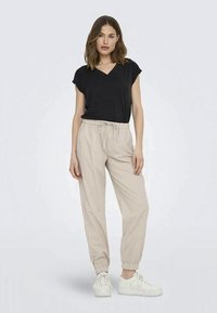 Black short-sleeve top with a V-neck, paired with beige tapered jogger pants and white sneakers. Smooth texture and elastic waistband.