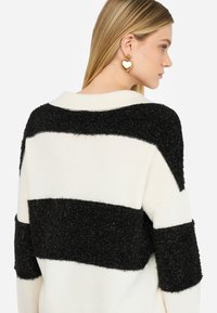 Maglione con righe orizzontali bianche e nere, caratterizzato da una lavorazione a maglia nera testurizzata e una base bianca morbida. Con colletto largo come dettaglio.
