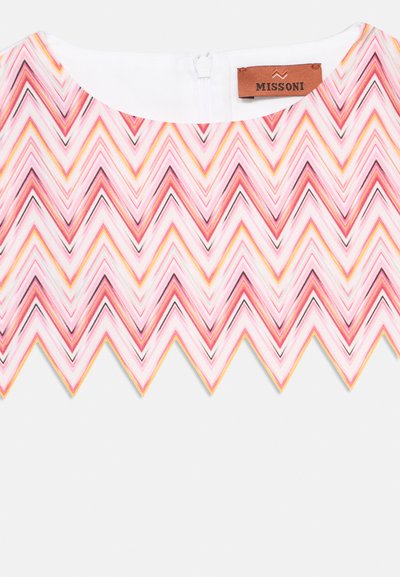 Gros plan sur un tissu à motifs zigzag rose, blanc et jaune avec un bord festonné et une étiquette Missoni marron sur un fond de fermeture éclair blanche.