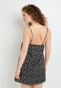 Abito nero con spalline sottili, caratterizzato da un motivo a pois in crema. Tessuto morbido con una vestibilità comoda e design con schiena scoperta.