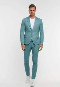 Helles blaues Anzug mit passgenauer Verarbeitung, bestehend aus einem Blazer mit einem Knopf, maßgeschneiderten Hosen und einem weißen T-Shirt. Die Schuhe sind weiße Sneakers.