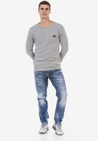 Grauer Langarmpullover mit strukturiertem Zickzackmuster, kombiniert mit hellblauen, verwaschenen Jeans. Sneakers runden das Outfit ab.