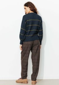 Pull marine à rayures jaunes, manches bouffantes et ourlet côtelé, porté avec un pantalon à carreaux marron et des chaussures beige à lacets.