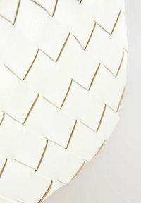 Matériau en cuir tissé blanc avec des pièces découpées rectangulaires aux bords dorés, créant un motif texturé et une forme arrondie.