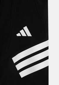 Svarta träningsshorts med en vit logotyp med tre ränder och en vinklad triangel-design på sidan. Texturerad tygsynlighet.