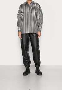 Chemise à manches longues rayée noir et blanc ; devant boutonné et coupe décontractée. Pantalon jogger en cuir noir avec poignets élastiques et bottes épaisses noires.