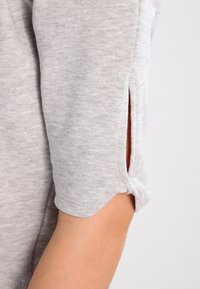Top de algodón gris con mangas hasta los codos, aberturas laterales, puños enrollados y un acabado suave y texturizado.