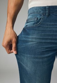 Donkerblauwe denim jeans met een aansluitend ontwerp, voorzien van een voorzak, subtiele verticale textuur en een zichtbare tailleband.