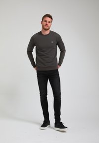 Maglietta a maniche lunghe grigia scura con motivo testurizzato, scollo tondo e una piccola toppa con logo. Abbinata a jeans neri slim e sneaker nere.