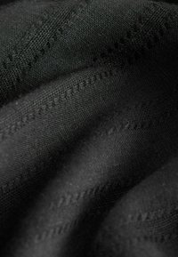 Tissu noir avec motifs en zigzag texturés diagonaux et armure visible, présenté en plis doux.