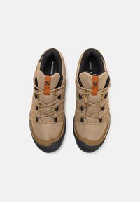 Light brown mesh hiking shoes with black rubber soles, featuring a lace-up design and an orange accent tab on the tongue.