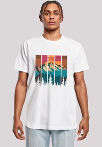 Witte katoenen t-shirt met een grafisch ontwerp van bergen en dennenbomen, met kleuren zoals teal, oranje, roze en bruine strepen.