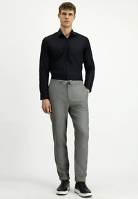 Zwart overhemd met knopen, grijze taps toelopende broek met trekkoord in de taille en zwarte sneakers met witte zolen. Eenvoudig ontwerp en gladde textuur.