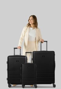 Trois valises noires de tailles variées, fabriquées dans un matériau texturé, dotées de poignées télescopiques et de roues à roulement fluide.