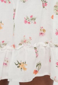 Λευκό ύφασμα με floral σχέδιο σε ροζ, πορτοκαλί και πράσινο. Διαθέτει βολάν στο τελείωμα και ελαφριά, υφή με ανάγλυφη αίσθηση.