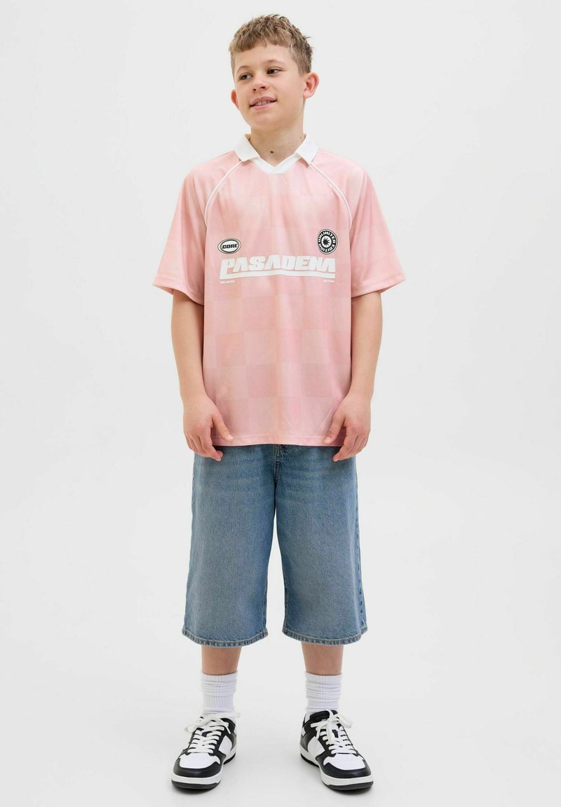 Camiseta de fútbol de manga corta color rosa claro con cuello blanco y logo, combinada con pantalones cortos de mezclilla azules y holgados, y zapatillas blancas y negras.