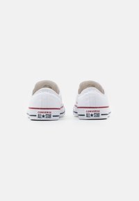 Bílé plátěné slip-on tenisky s gumovou podrážkou, zdobené červenými a modrými pruhy a logem "CONVERSE ALL STAR" na patě.