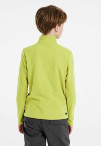 Pullover in pile verde con un colletto alto, maniche lunghe e una superficie testurizzata. L'orlo è leggermente curvo e presenta un piccolo etichetta con logo in basso.