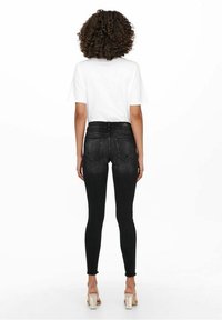 Pantalones vaqueros skinny de tiro alto en negro con dobladillo deshilachado, con costuras en contraste y dos bolsillos traseros. Combinados con una camiseta blanca sencilla.