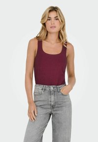 Bordeaux nederdel med rund hals, lavet af blødt stof, parret med lysegrå højtaljede jeans med forlommer.