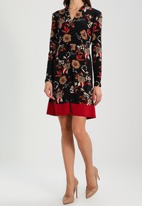 Černé květinové šaty s dlouhými rukávy, se červenými akcenty na lemu. Navrženy s různými květinovými vzory a výstřihem do V.