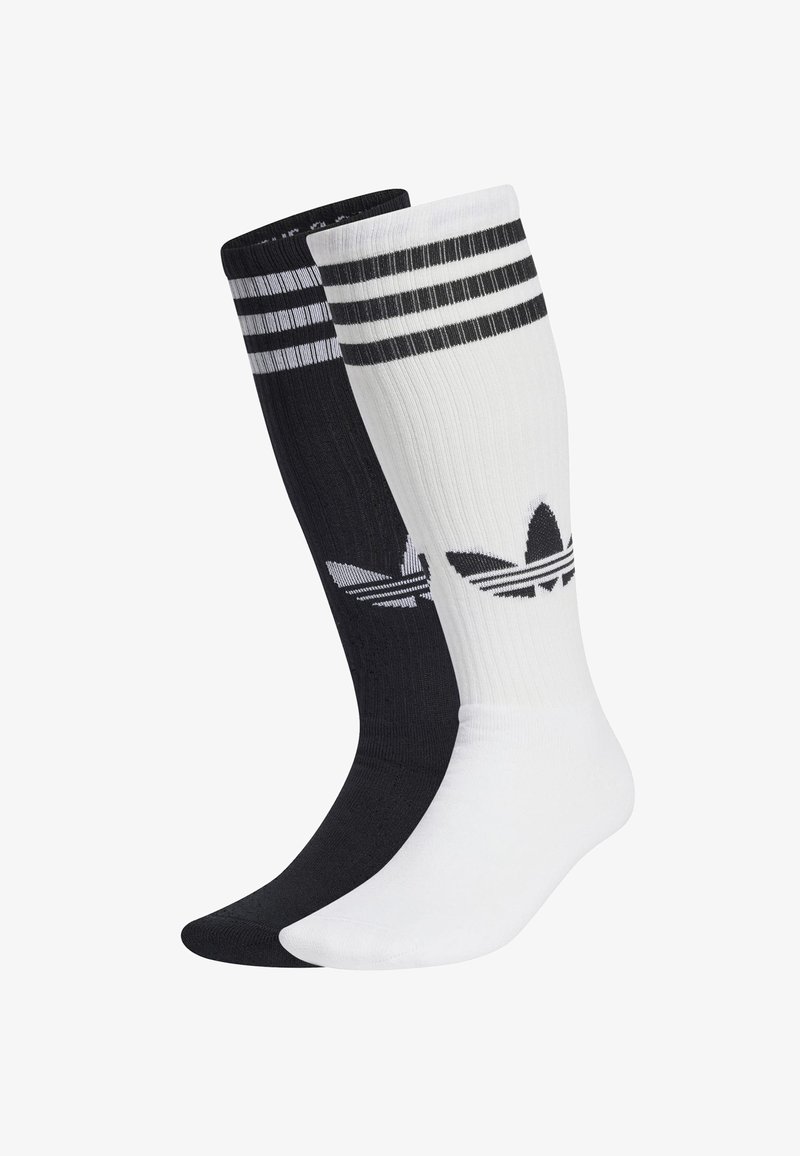 Kaksi paria polvipituista sukkia, toinen musta ja toinen valkoinen. Kummassakin on kolme vaakasuoraa raitaa ylhäällä ja Adidas-logo.