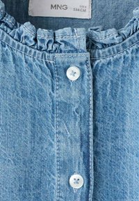 Top in denim bluastro con colletto arricciato, chiusura frontale con bottoni e dettagli in bottoni bianchi. Il tessuto presenta una leggera texture e una sfumatura.