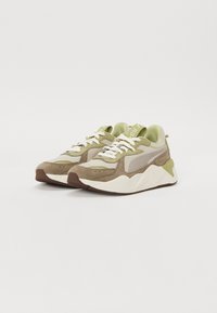 Pantofi sport cu un amestec de întărituri de suede bej deschis și închis, cu accente verzi, șireturi albe, o talpă texturată și un design robust și sportiv.