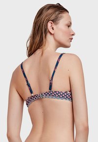 Top bikini floreale blu navy con spalline sottili e regolabili, caratterizzato da una fascia decorata e una chiusura sul retro. Dettaglio con bordo scallop.