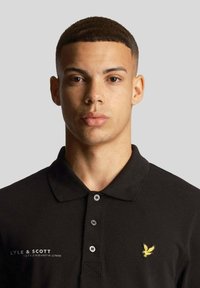 Polo shirt nera in cotone, con un logo ricamato in oro sulla parte sinistra del petto e un'apertura con tre bottoni neri.