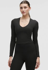 Top negru cu mâneci lungi, cu decolteu adânc în V, realizat dintr-un material ribbed. Prezentând o siluetă ajustată și o textură moale, este completat de un finisaj neted.