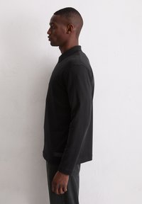 Zwart poloshirt met lange mouwen en een kraag, voorzien van een rechte zoom en een subtiel label linksonder. Zachte, gladde katoenen stof.