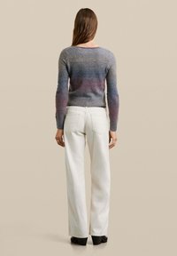 Handgestrickter Pullover mit einem Farbverlauf von Grau zu Lila, mit langen Ärmeln und geripptem Saum, kombiniert mit weißen weit geschnittenen Hosen.