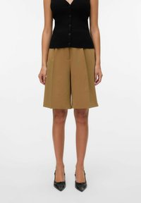 Zwarte geribbelde knooploze tanktop gecombineerd met bruine high-waisted shorts, met een gestructureerde wijde pijp en een gladde stof. Zwarte puntige hakken.