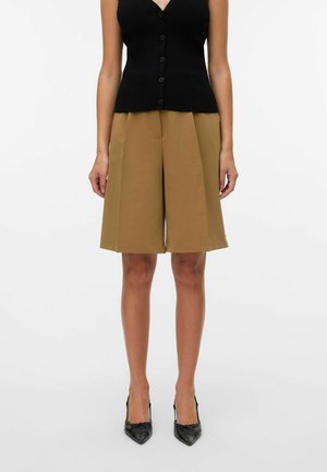 Débardeur noir à côtes avec boutons, associé à un short taille haute marron, structuré avec une jambe large et un tissu lisse. Talons aiguilles noirs.