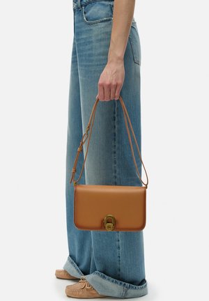 Sac à main en cuir marron avec un fermoir doré, de forme rectangulaire et avec une bandoulière amovible. Le sac a une texture lisse et un design minimaliste.